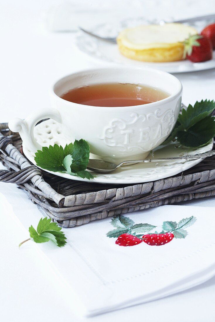 Eine Tasse Tee auf Korbtablett und Serviette mit Erdbeermotiv