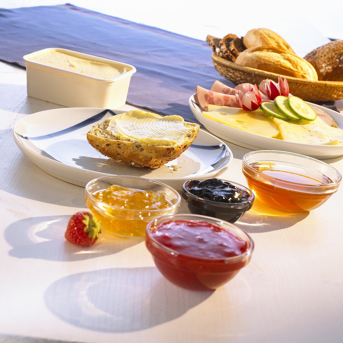 Frühstück mit Marmelade, Wurst, Käse und einem Korb voller Brötchen