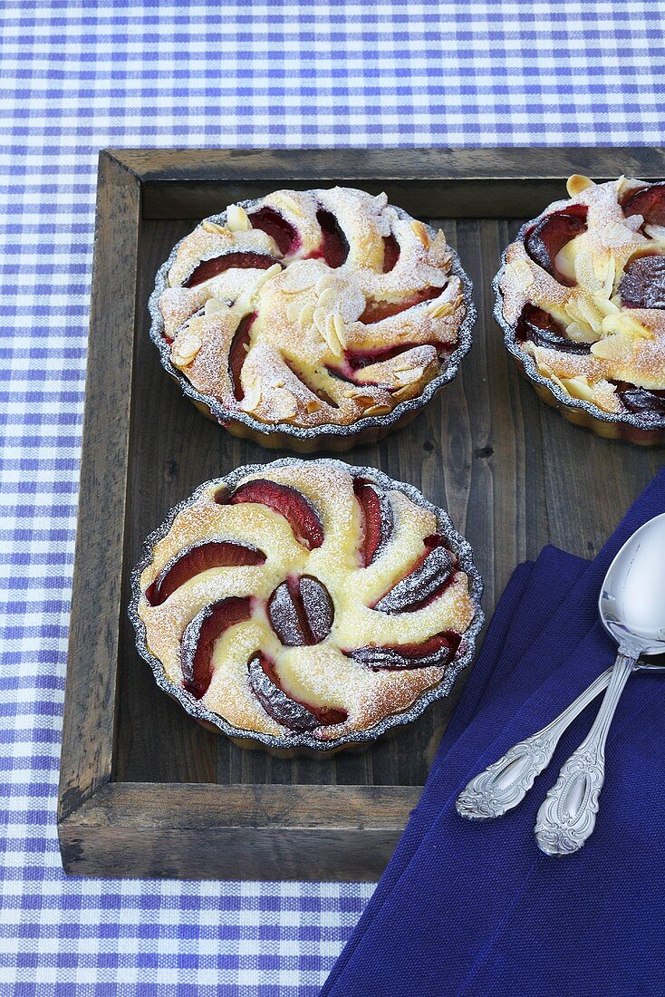 Plum tartlets in glass bowls on a wooden tray
