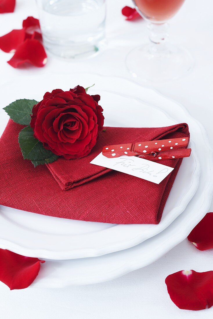 A place setting with a red napkin and a rose