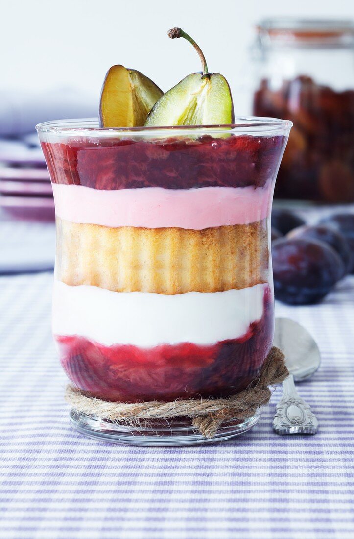 A layered dessert consisting of plum compote, sponge cake and quark served in a glass