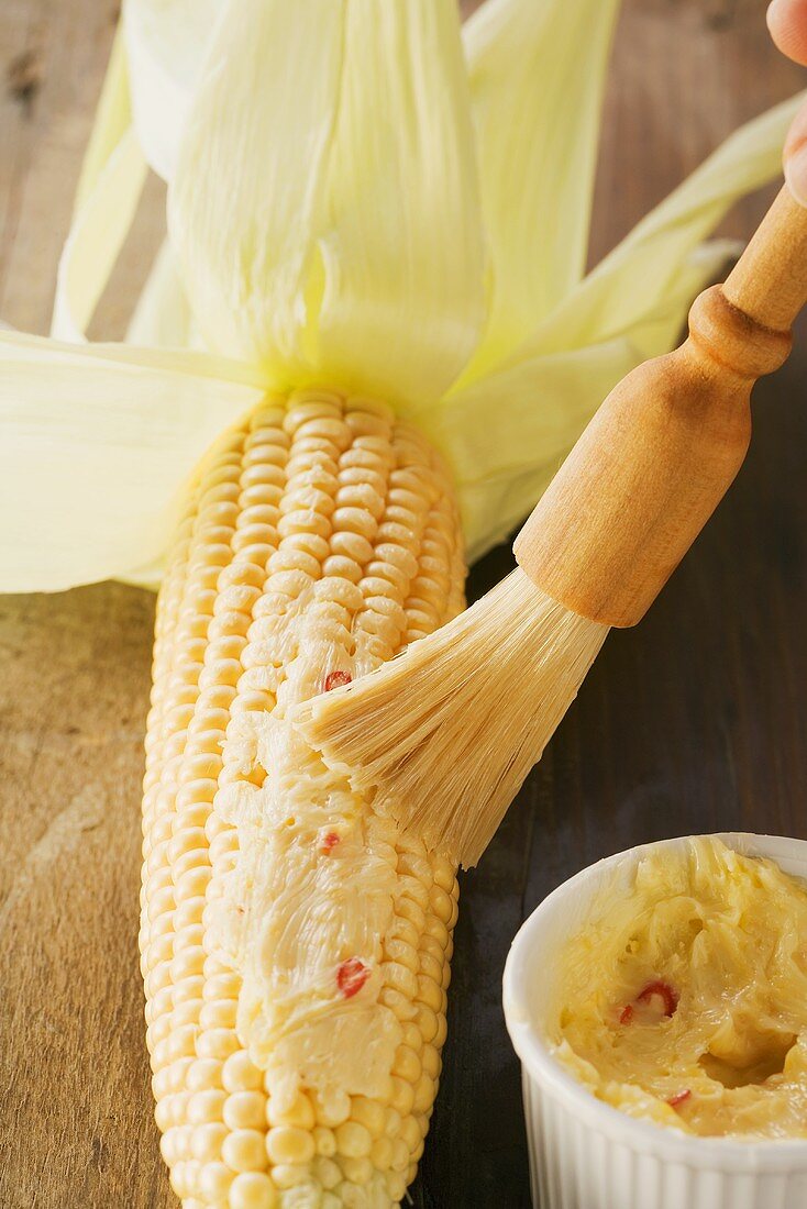 Maiskolben mit Chili-Zitonen-Butter bestreichen