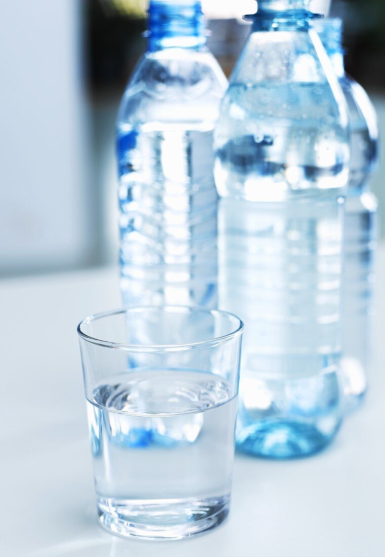 Wasserglas und drei Wasserflaschen im Hintergrund