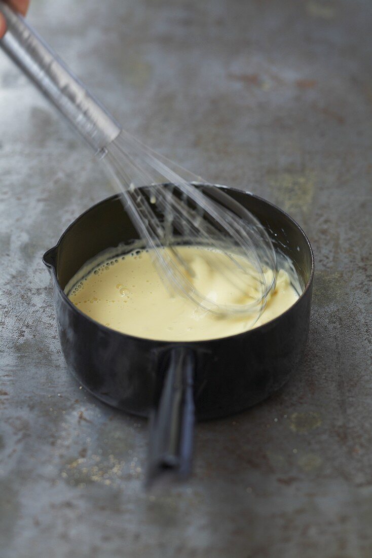Stirring butter into white wine cream sauce with whisk