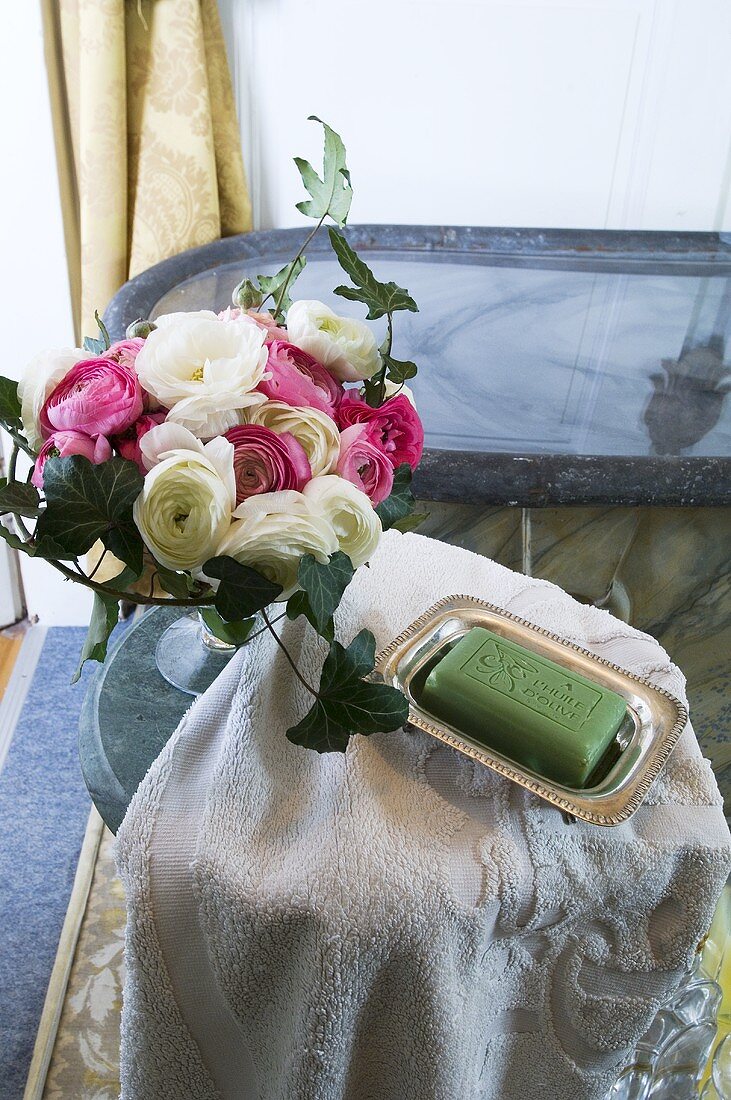 Bath towel, soap and vase of ranunculus in a bathroom