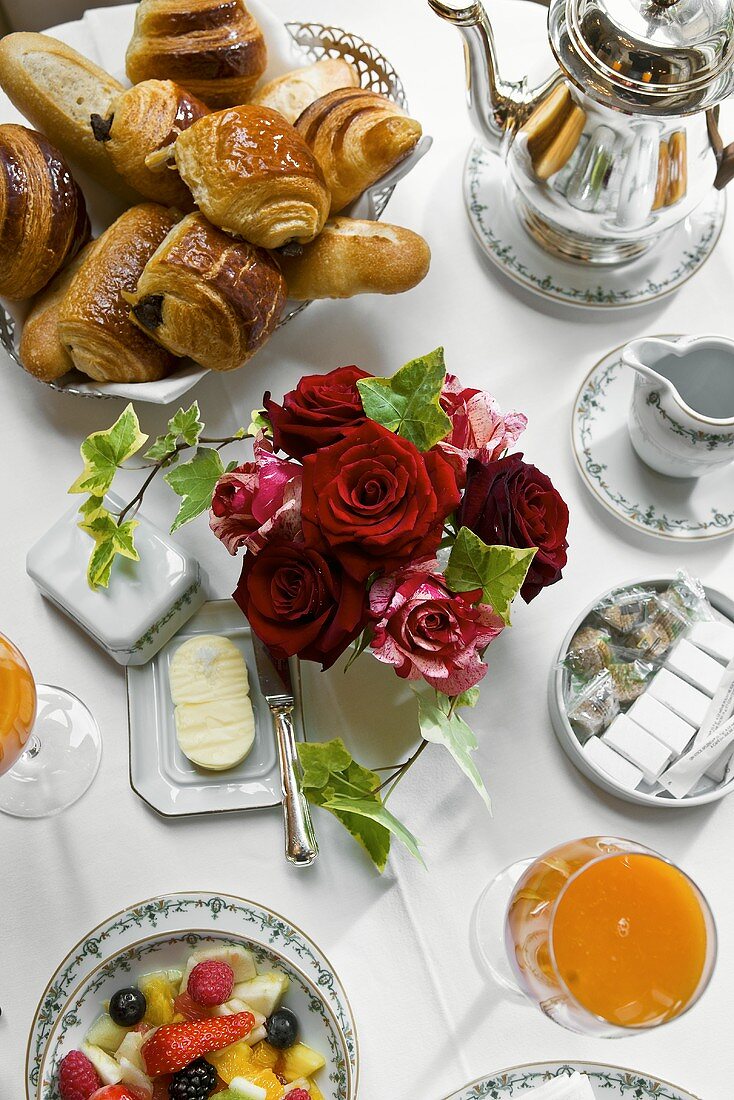 Frühstückstisch mit Gebäck, Kaffeekanne, Rosen, Saft und Obstsalat