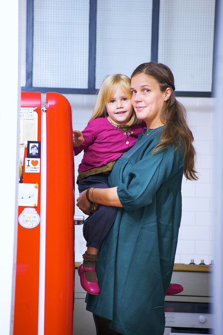 Mutter mit kleiner Tochter auf dem Arm neben Kühlschrank