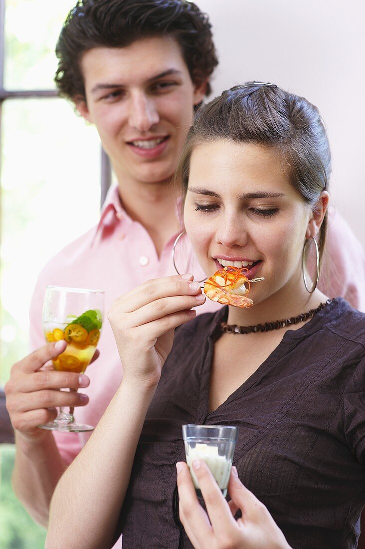Woman eating chilli prawns, man holding drink at tapas buffet
