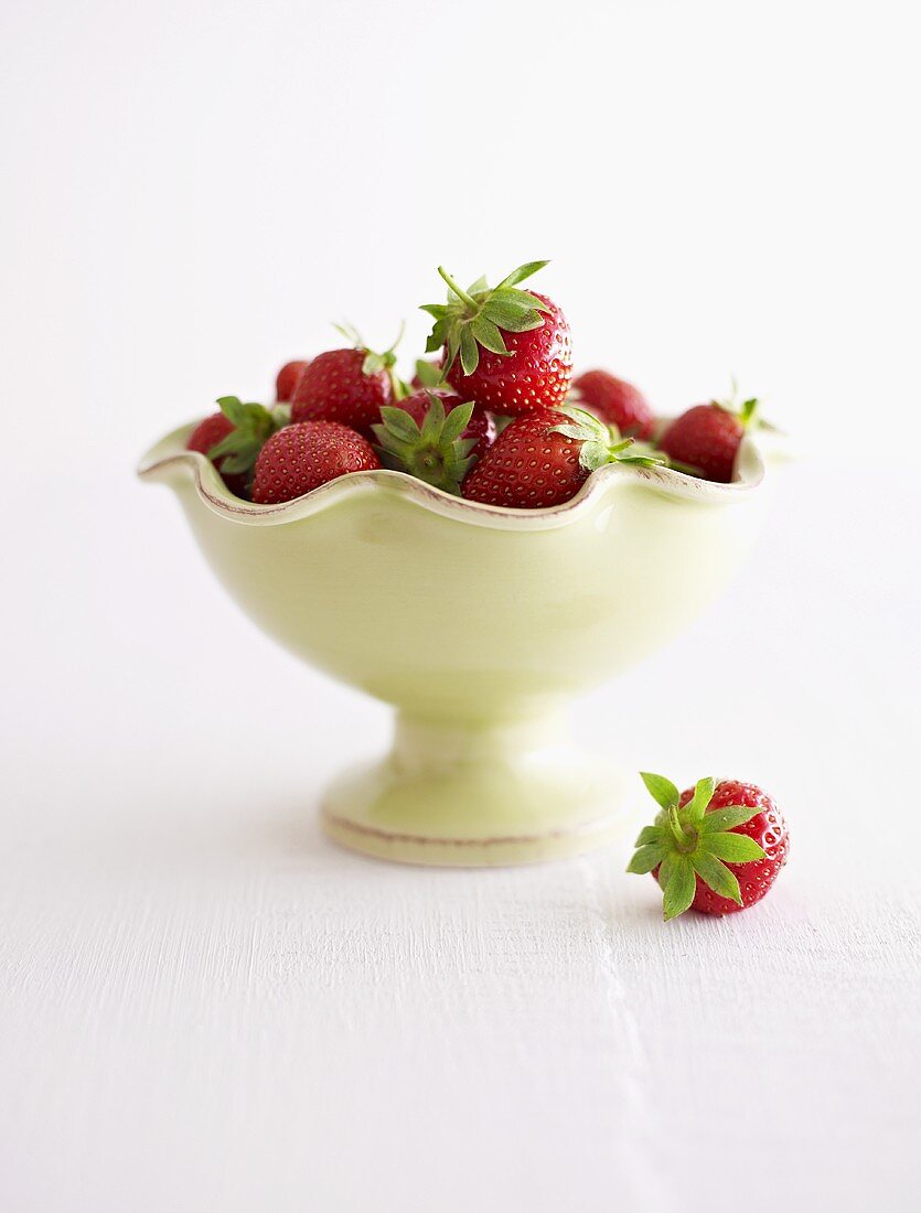 Fresh strawberries in and beside pedestal bowl