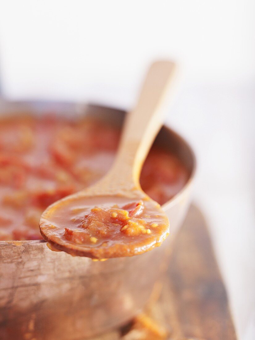 Tomatensauce auf Kochlöffel und im Topf