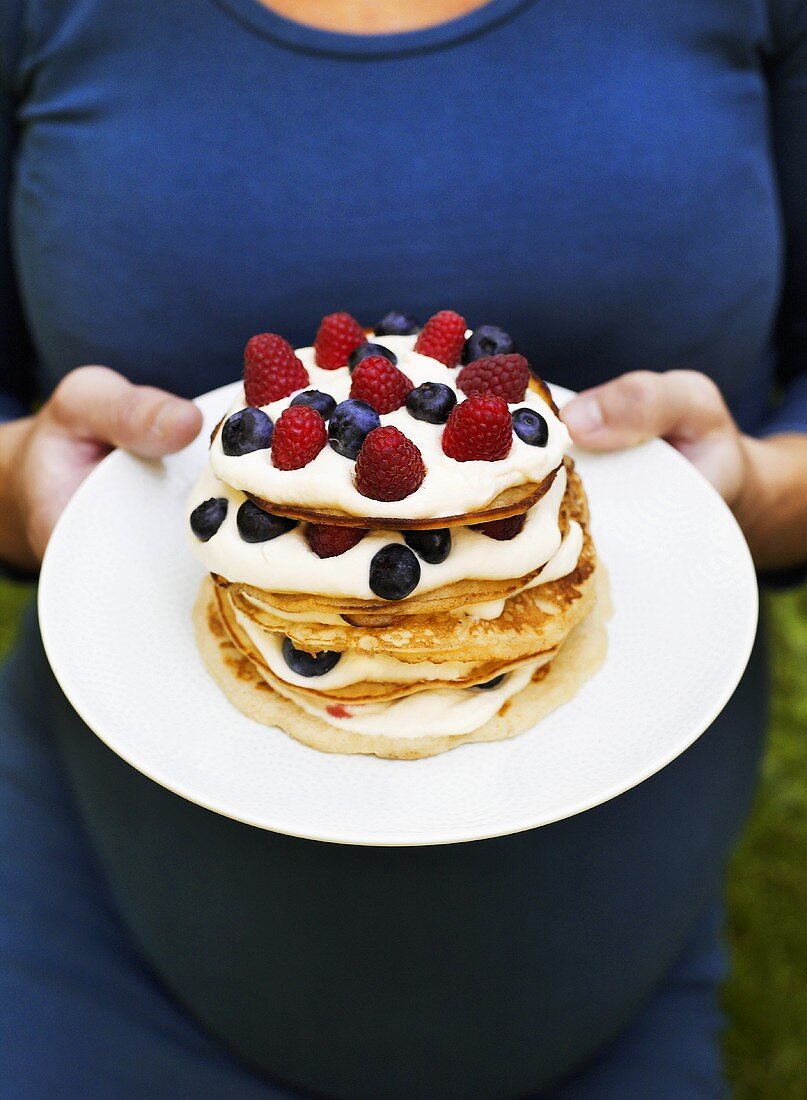 Woman holding pancakes with cream and berries