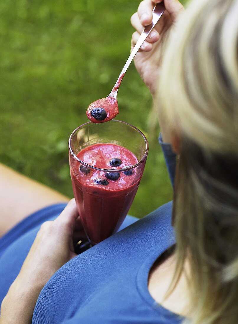 Frau isst Himbeersmoothie mit Heidelbeeren