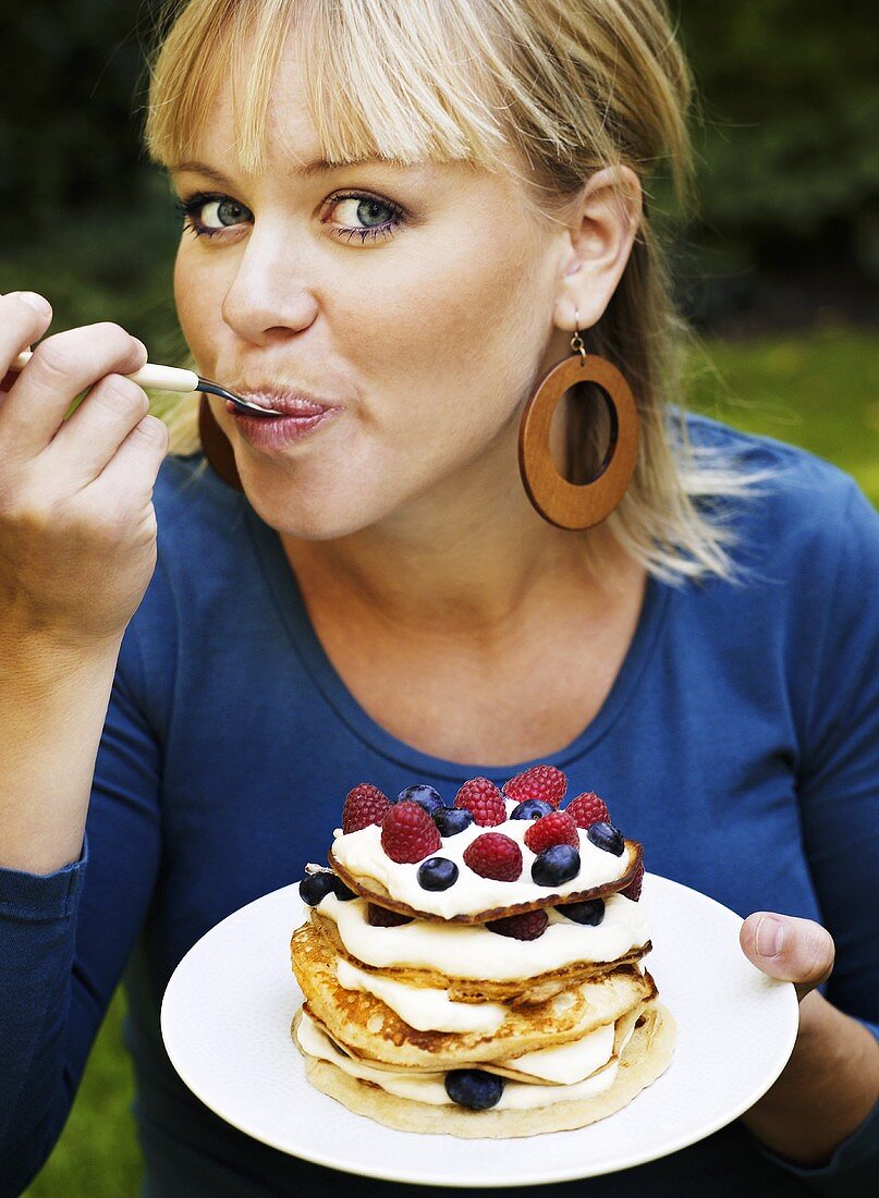 Frau isst Pancakes mit Sahne und Beeren