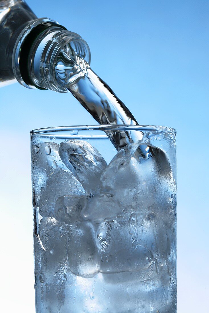 Wasser in Glas mit Eiswürfeln gießen