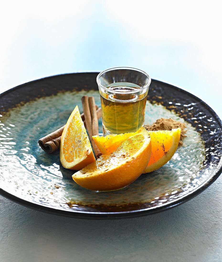 Glass of tequila with cinnamon and oranges on plate