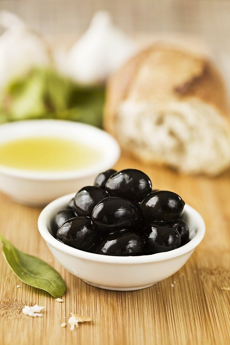 Black olives in dish, olive oil, white bread