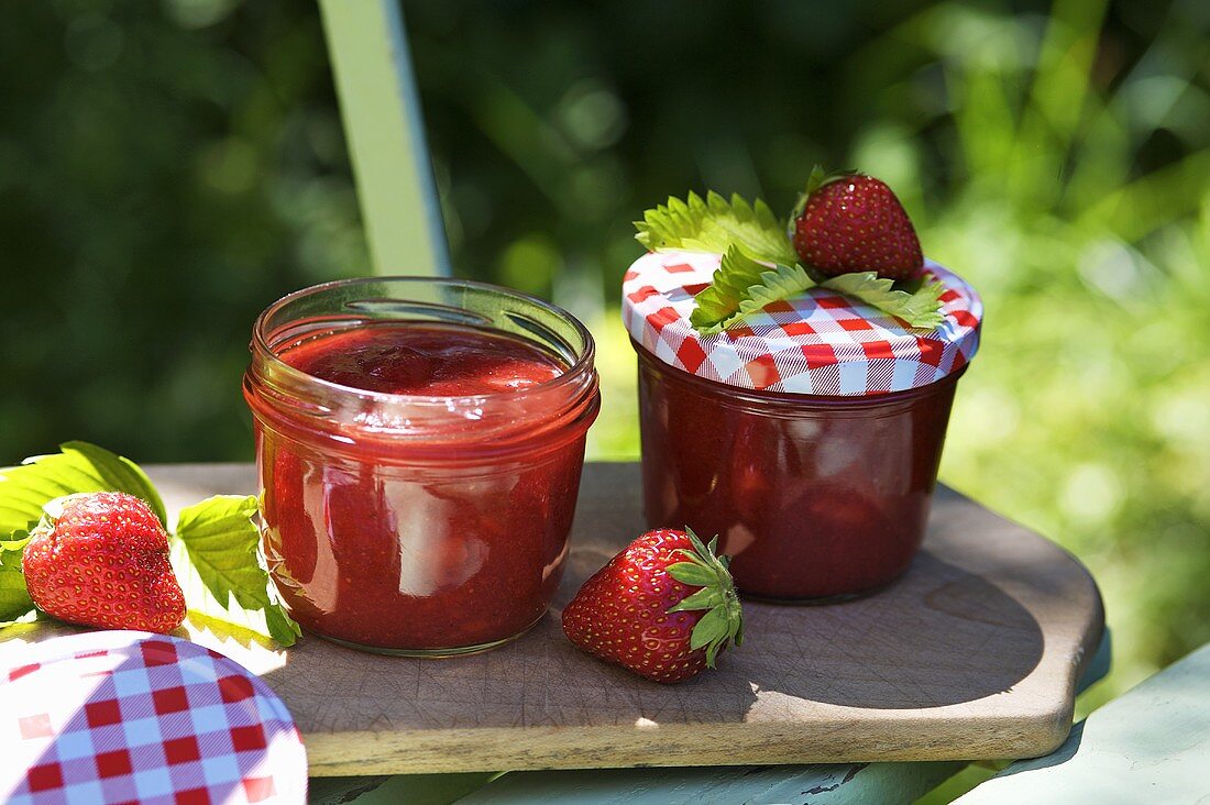 Two jars of strawberry jam & fresh strawberries on chopping board