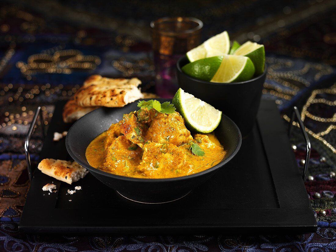 Chicken curry with lime wedges and flatbread (India)