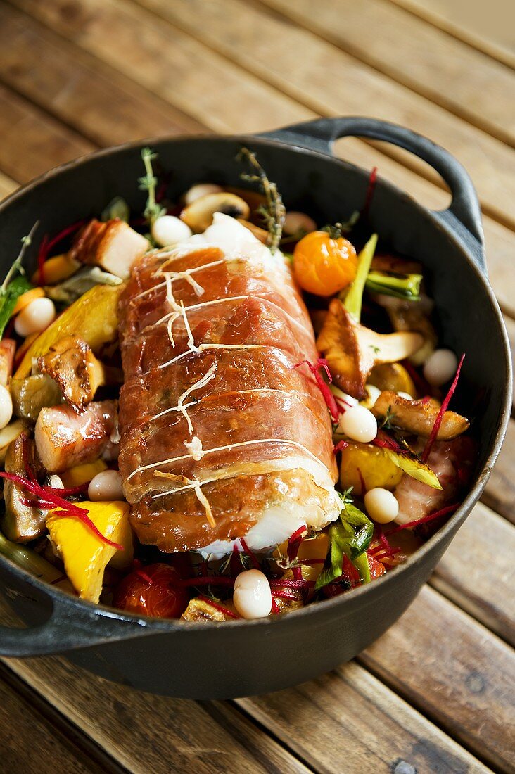 Bacon-wrapped cod on vegetables in pan