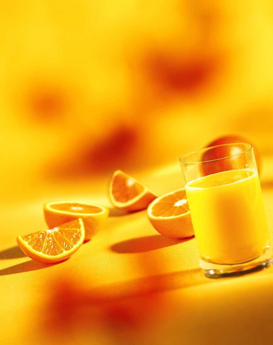 A glass of orange juice, orange halves and wedges
