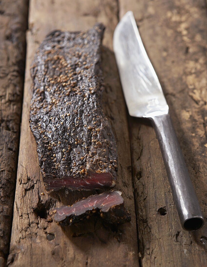Biltong (getrocknetes Rindfleisch, Südafrika) auf Holzuntergrund mit Messer
