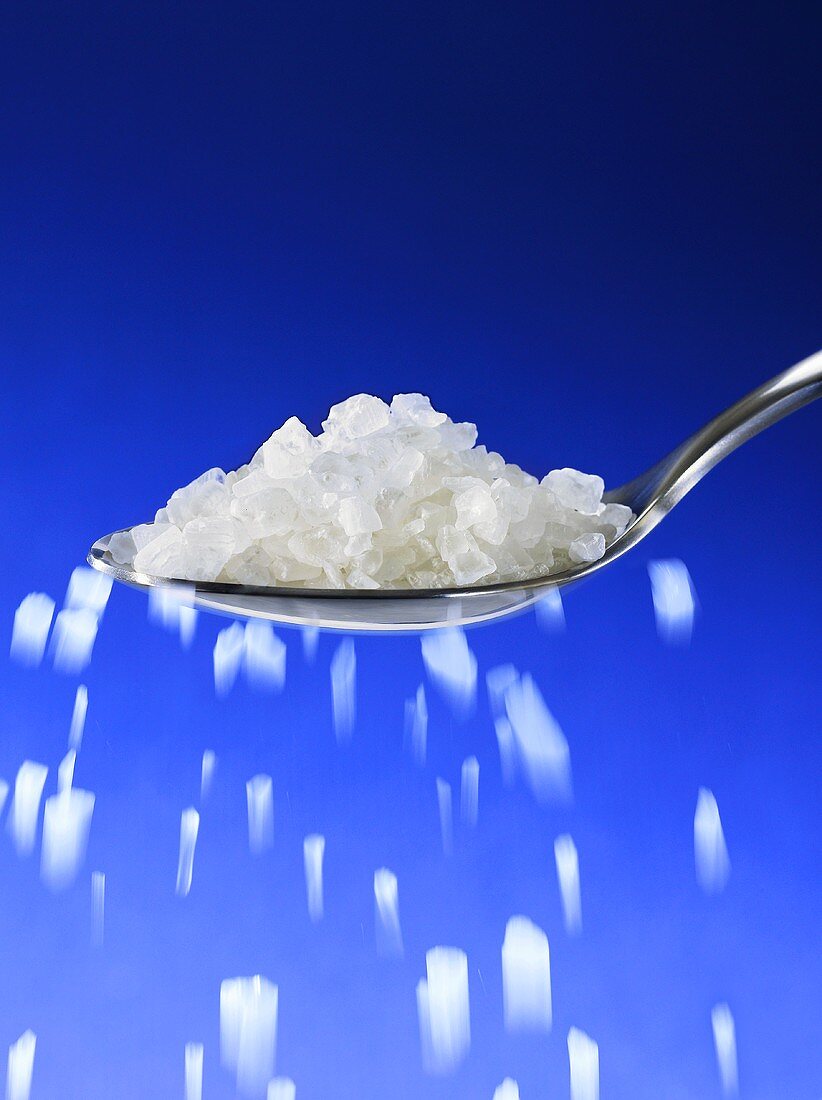 Sea salt trickling from spoon against blue background