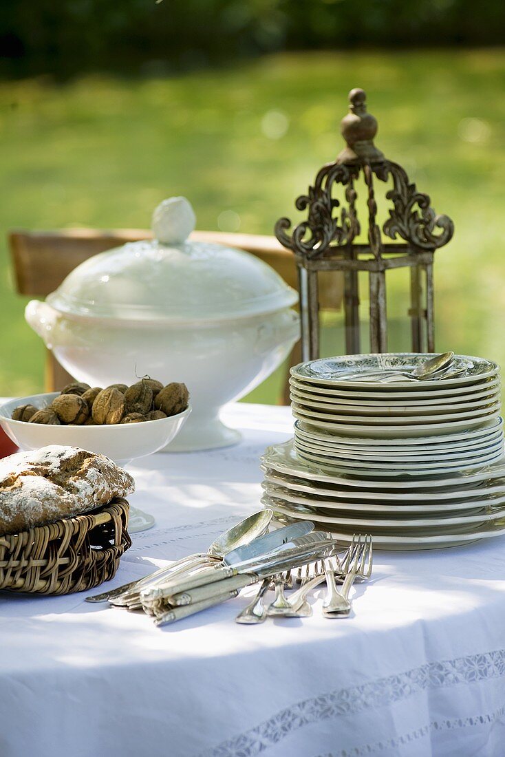 Geschirr, Besteck, Brot und Nüsse auf Tisch im Garten