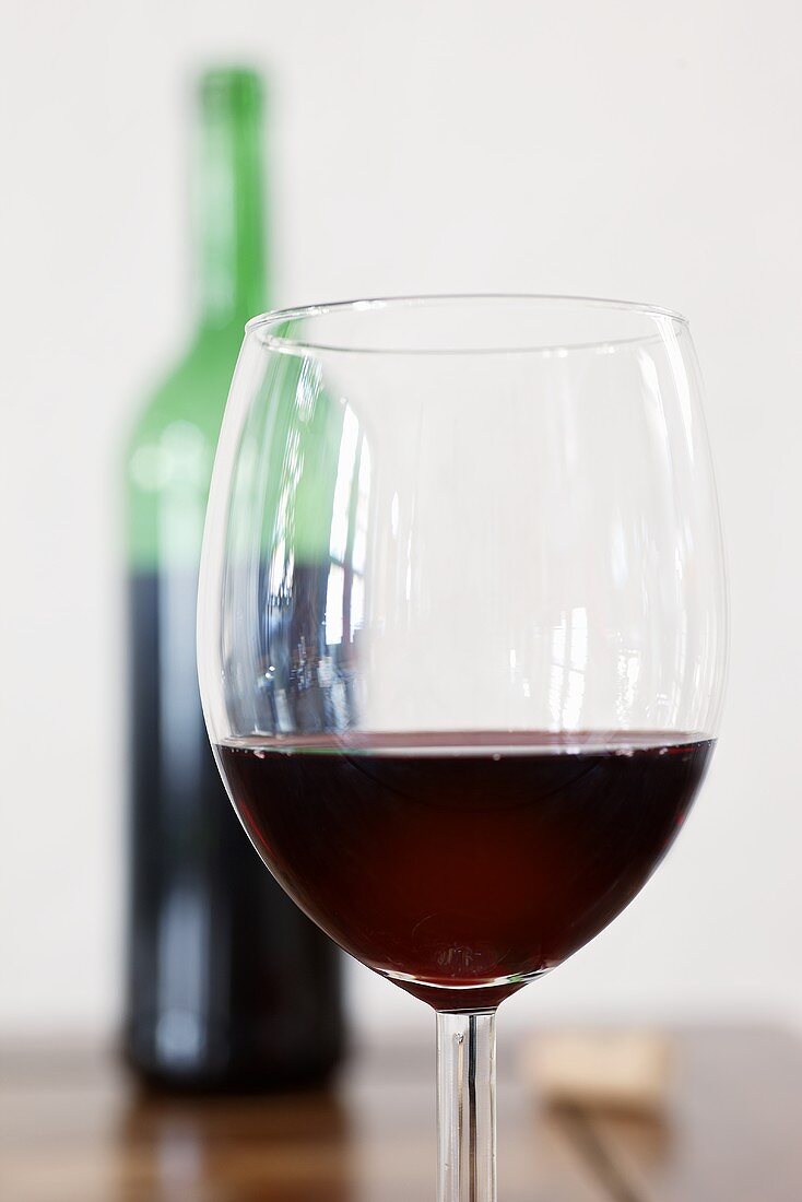 A glass of red wine, red wine bottle in background