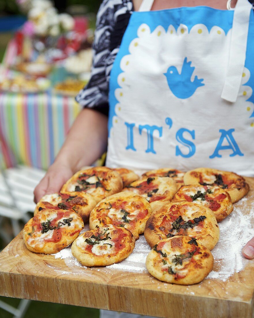 Frau hält Holzbrett mit Mini-Pizzen