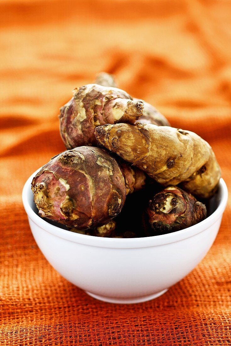 Jerusalem artichokes in bowl on orange background