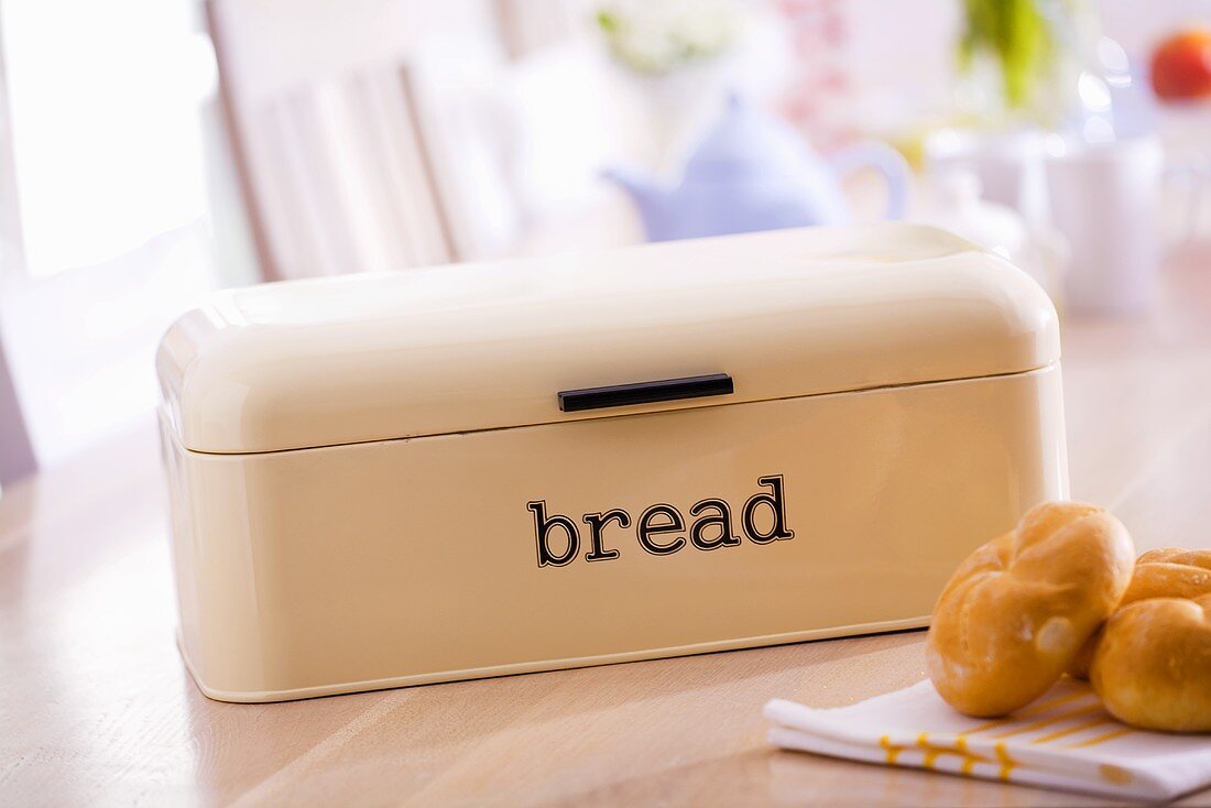 Bread bin and bread rolls on breakfast table