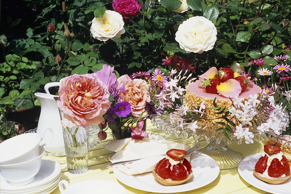 Strawberry tarts and cake in garden with fresh flowers