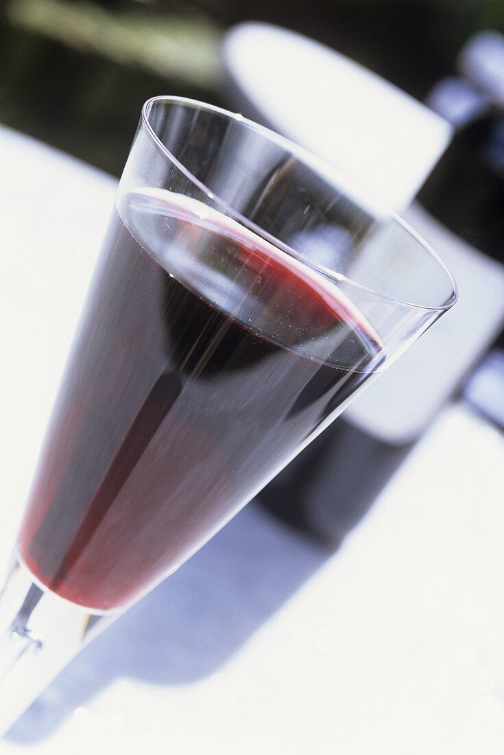 Glas Rotwein vor Weinflasche auf einem Gartentisch