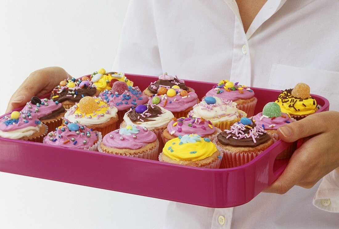 Frau hält pinkfarbenes Tablett mit Cupcakes