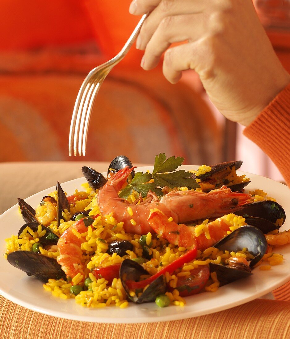 Hand with fork over a plate of paella