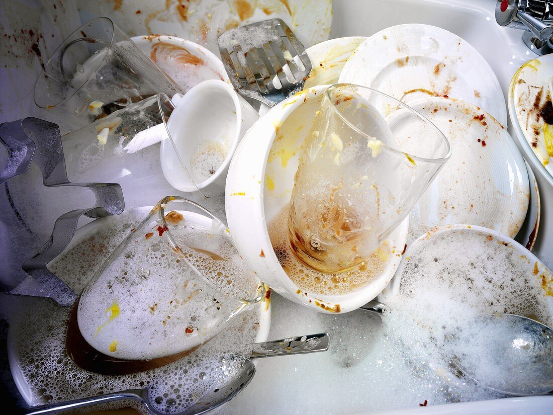 Dirty crockery in washing-up water in kitchen sink