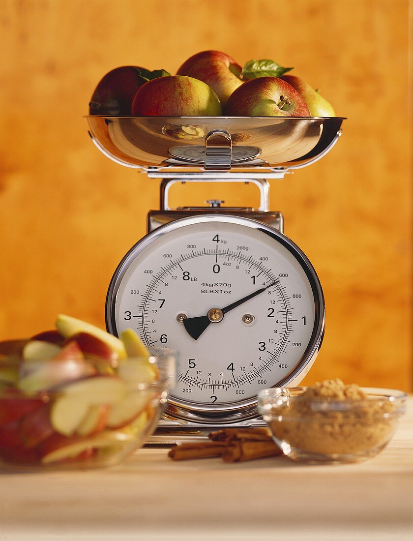 Apples on kitchen scales, apple slices, cinnamon & sugar in front