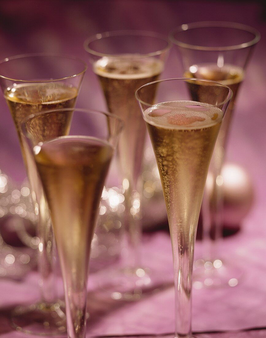 Fünf Champagnerflöten, im Hintergrund Weihnachtskugeln