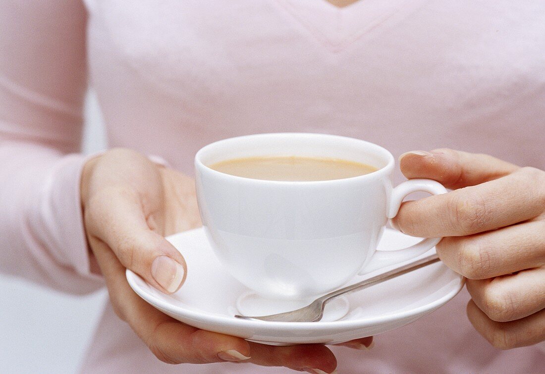 Frau hält eine Tasse schwarzen Tee mit Milch (Bildausschnitt)