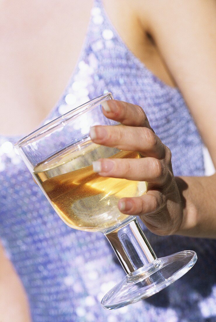 Frau im Partydress hält ein Glas Weißwein (Bildausschnitt)