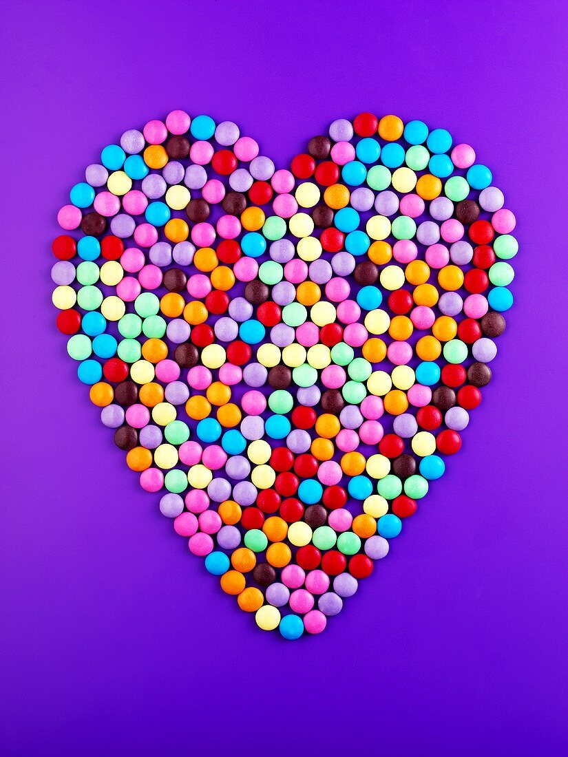 Chocolate beans forming heart on purple background