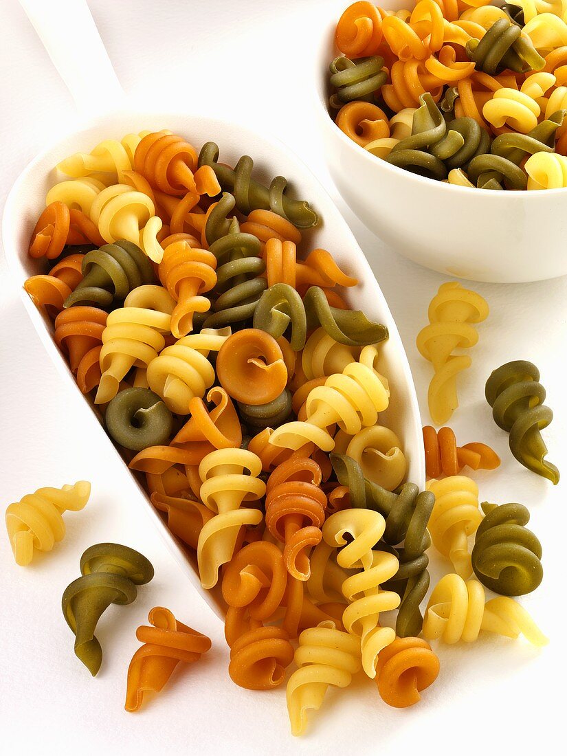 Coloured pasta spirals in scoop and bowl