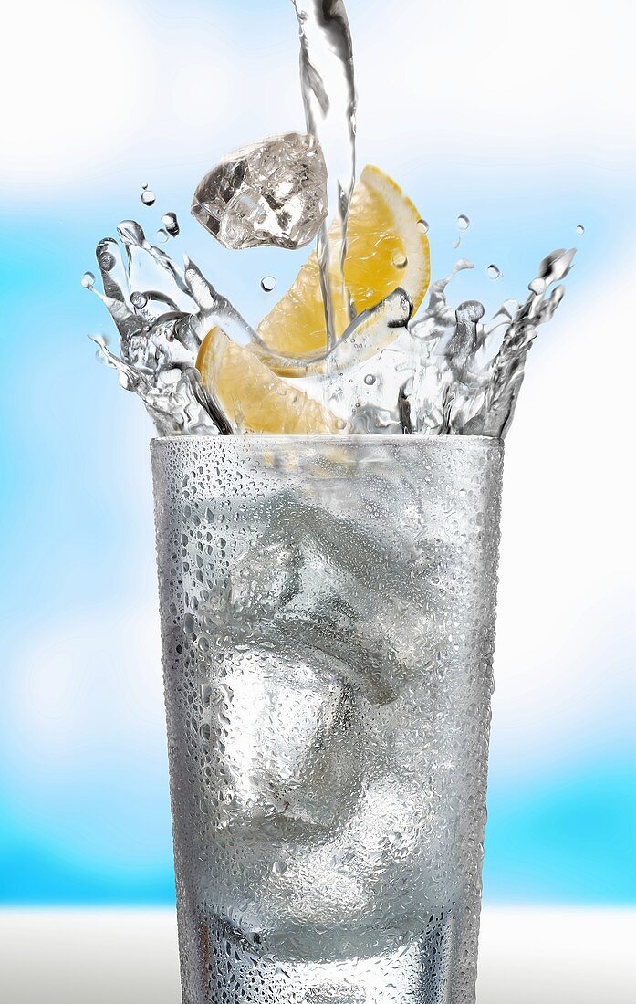 Ice cubes and lemon wedges falling into a glass of water