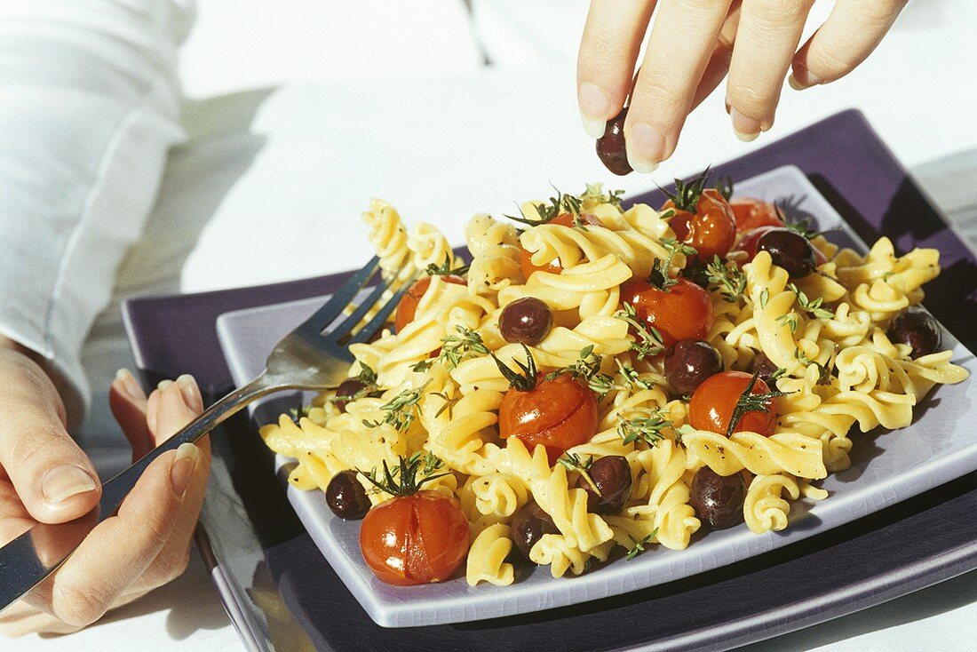 Hände über Nudelgericht mit Kirschtomaten und Oliven
