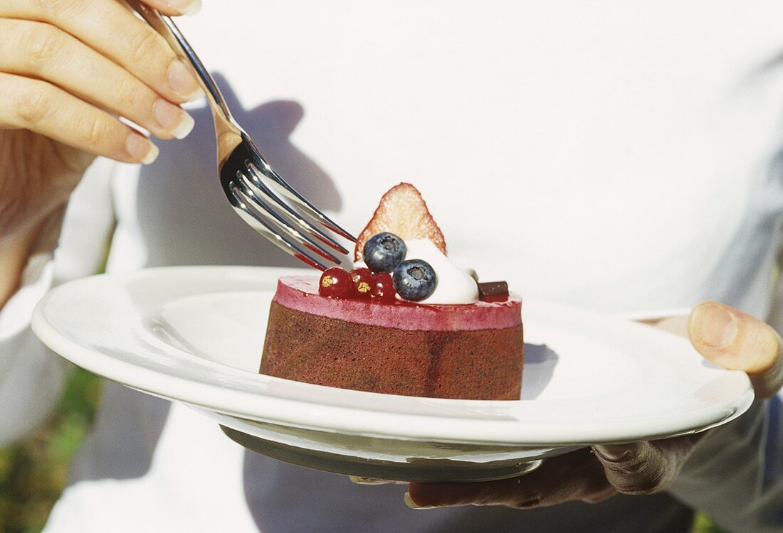 Woman eating small chocolate cake topped with berry mousse