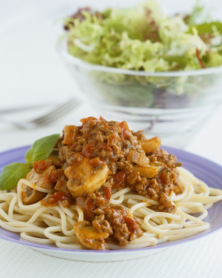Spaghetti Bolognese mit Champignons, dahinter Salat