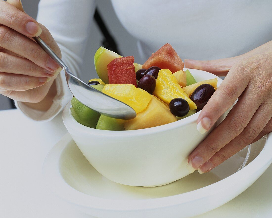 Woman eating fruit salad out of a small bowl