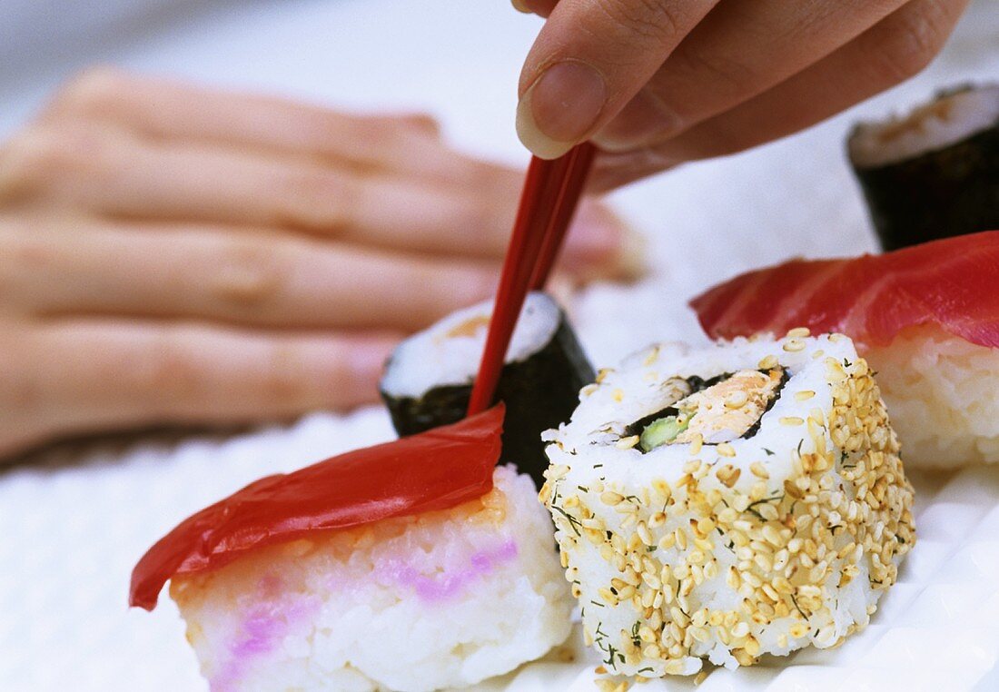 Hand hält Sushi mit Essstäbchen