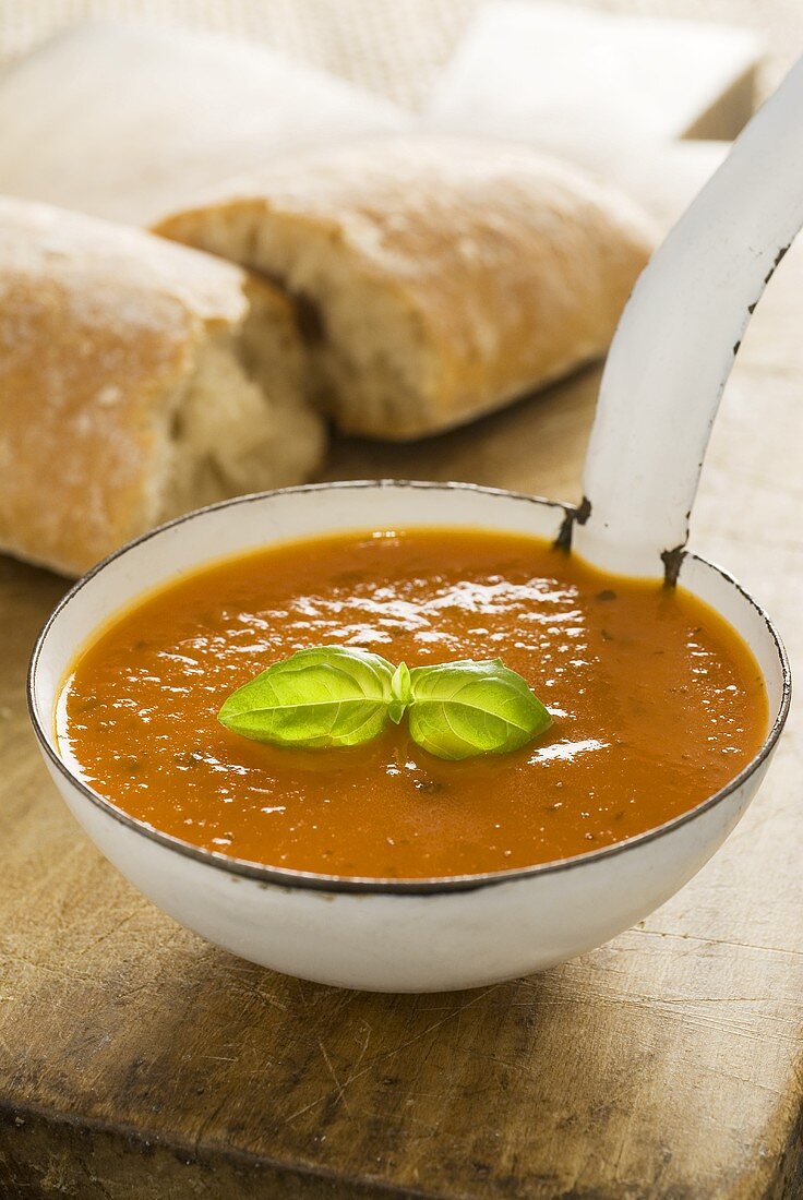 Tomato soup in ladle with ciabatta in background