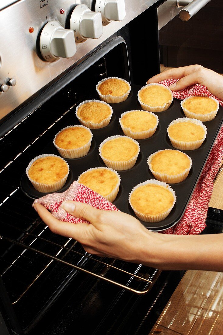 Taking freshly baked cupcakes out of the oven